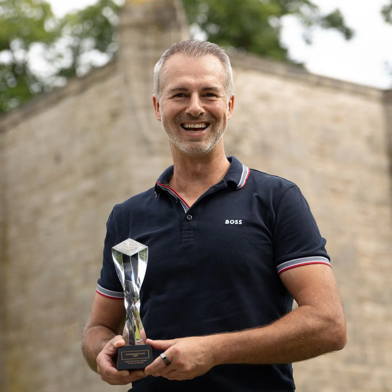 Enrico Barkusky von UnternehmerPlus® mit HIPE AWARD vor historischer Steinmauer